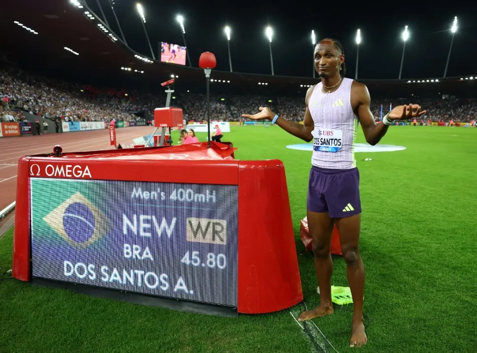 Alison dos Santos, o Piu, posa ao lado do quadro que mostra seu novo recorde mundial nos 400 metros com barreiras REUTERS/Denis Balibouse